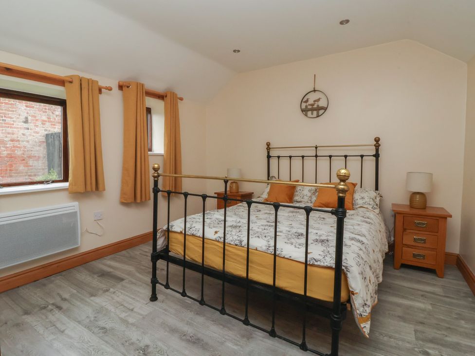 A bedroom with a bed, nightstands, and windows at Honeybee Cottage in Withernsea