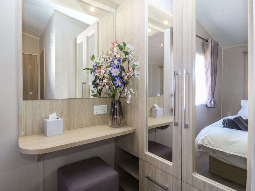 A bedroom with a mirror and flowers on a table at Pheasant Lodge in Holyhead
