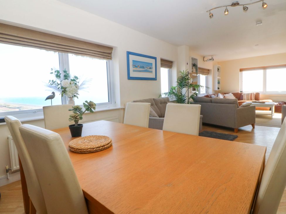 A dining room with a table and chairs overlooking the sea at Snowdonia View in Pwllheli