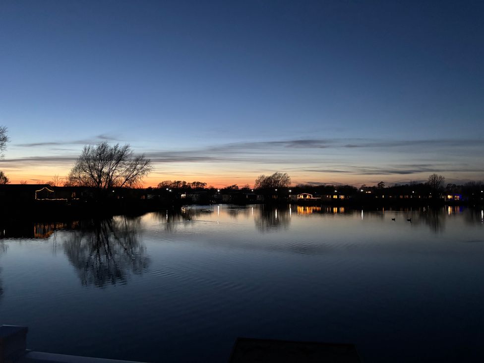 A view of a lake at sunset with trees and houses at Indulgence Fishing Lodge with Private Hot Tub Tattershall
