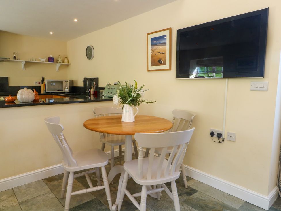 A kitchen with a table and chairs with a TV on the wall at Plas Tirion Cottage Mostyn near Holywell