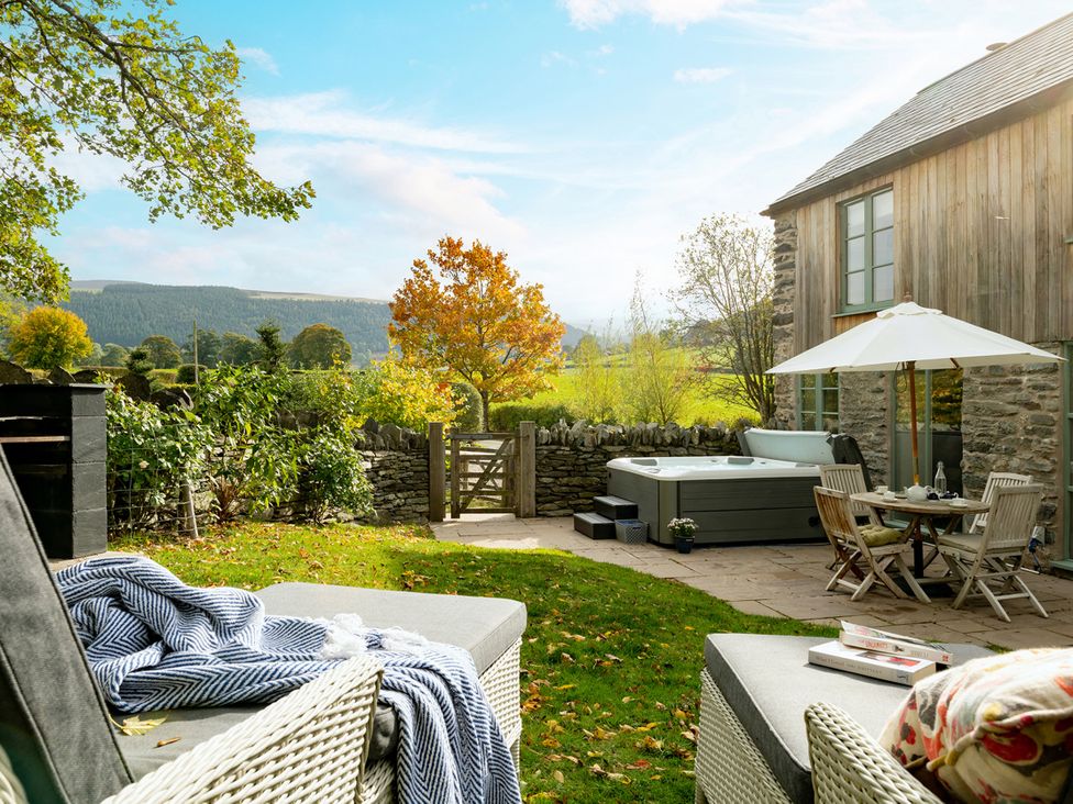 A garden with a hot tub and dining table at Shepherds Cottage in Llandrillo