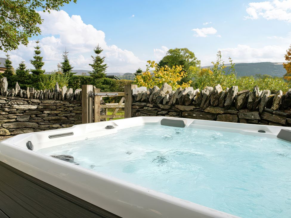 A hot tub surrounded by a stone wall and trees at Shepherds Cottage in Llandrillo
