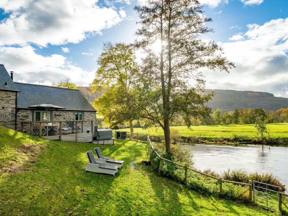 A cottage with a deck and chairs by the river at Flyfishers Cottage in Llandrillo