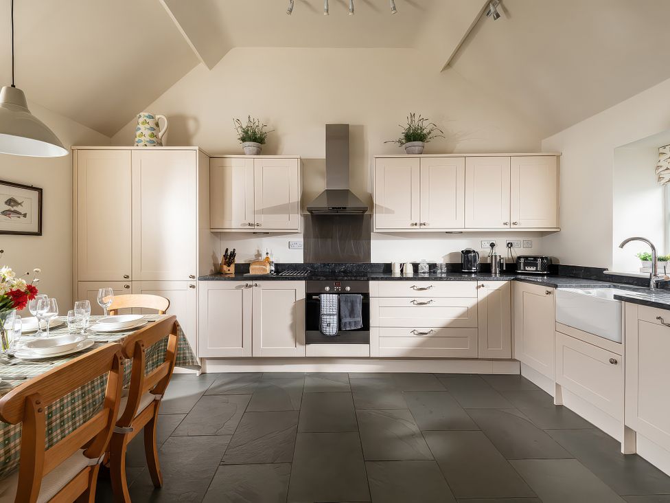 A kitchen with cabinets and a dining table at Flyfishers Cottage in Llandrillo
