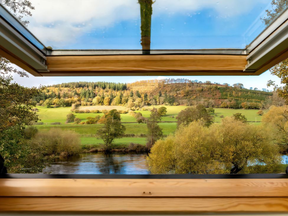 A window showing a view of trees and a river at Flyfishers Cottage in Llandrillo