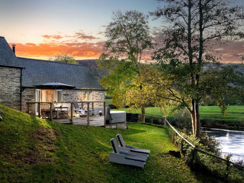 A house with a deck and chairs by a river at Flyfishers Cottage in Llandrillo