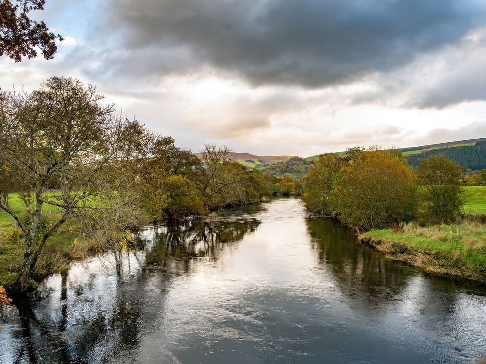 A river with trees and hills in the background at Flyfishers Cottage Llandrillo