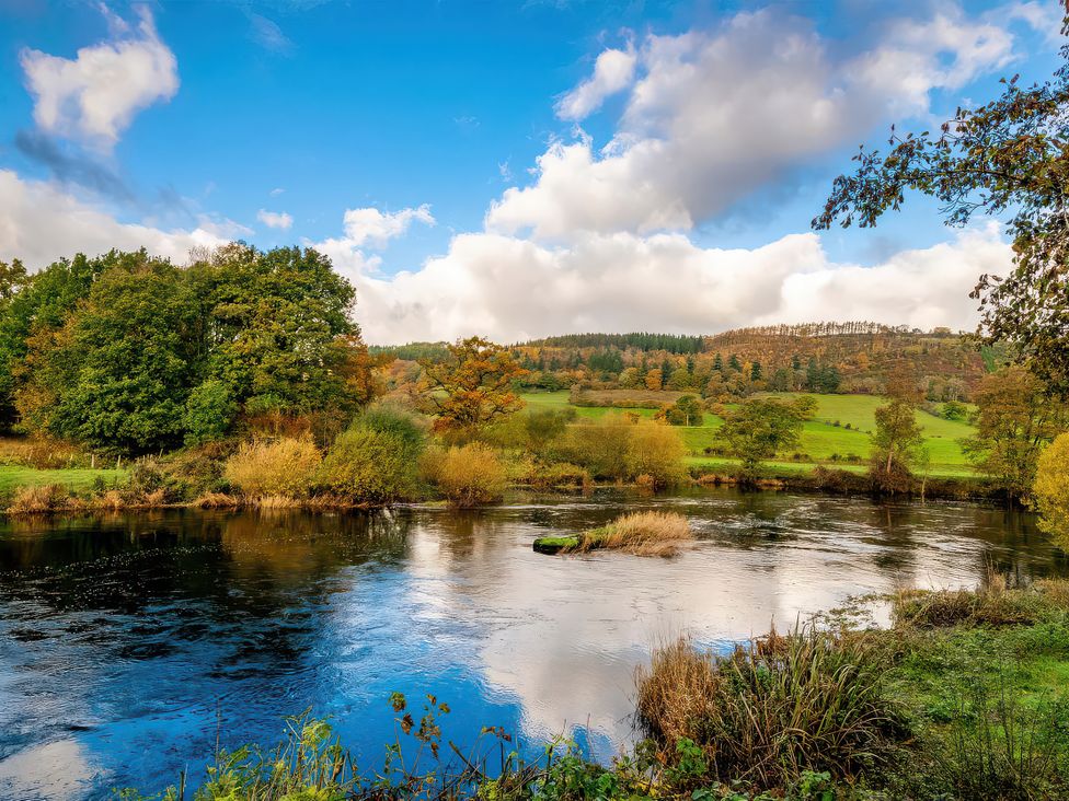 A river with trees and hills in the background at Flyfishers Cottage in Llandrillo