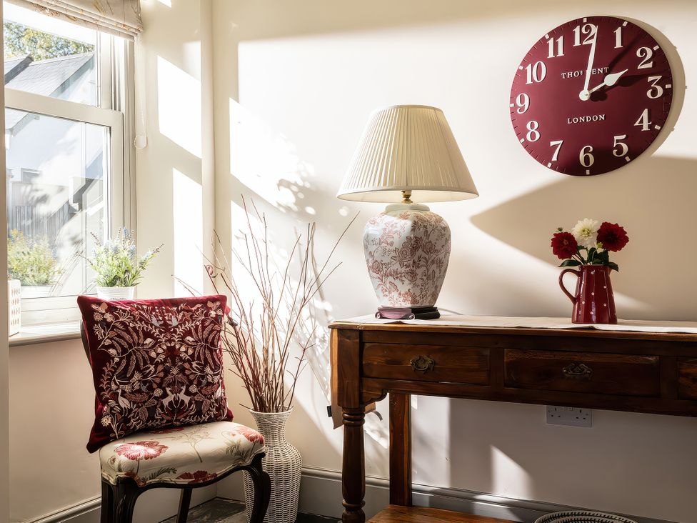 A room with a table, lamp, flowers, and a clock at Cilan Farmhouse in Llandrillo