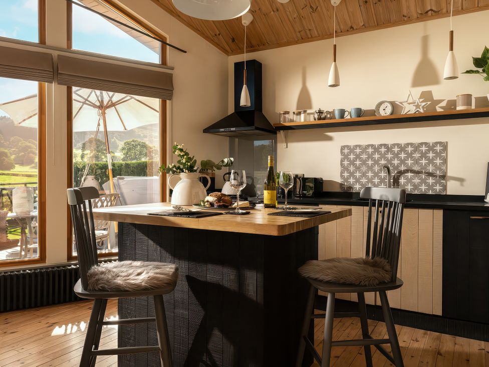 A kitchen with a dining table and bar stools at Lagom Log Cabin in Llandrillo