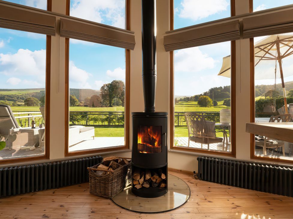 A living room with a wood stove and large windows at Lagom Log Cabin in Llandrillo