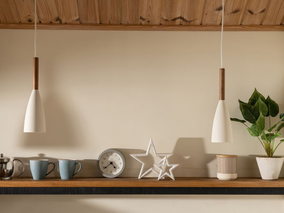A kitchen with a shelf holding cups, clock, stars, and a plant at Lagom Log Cabin, Llandrillo
