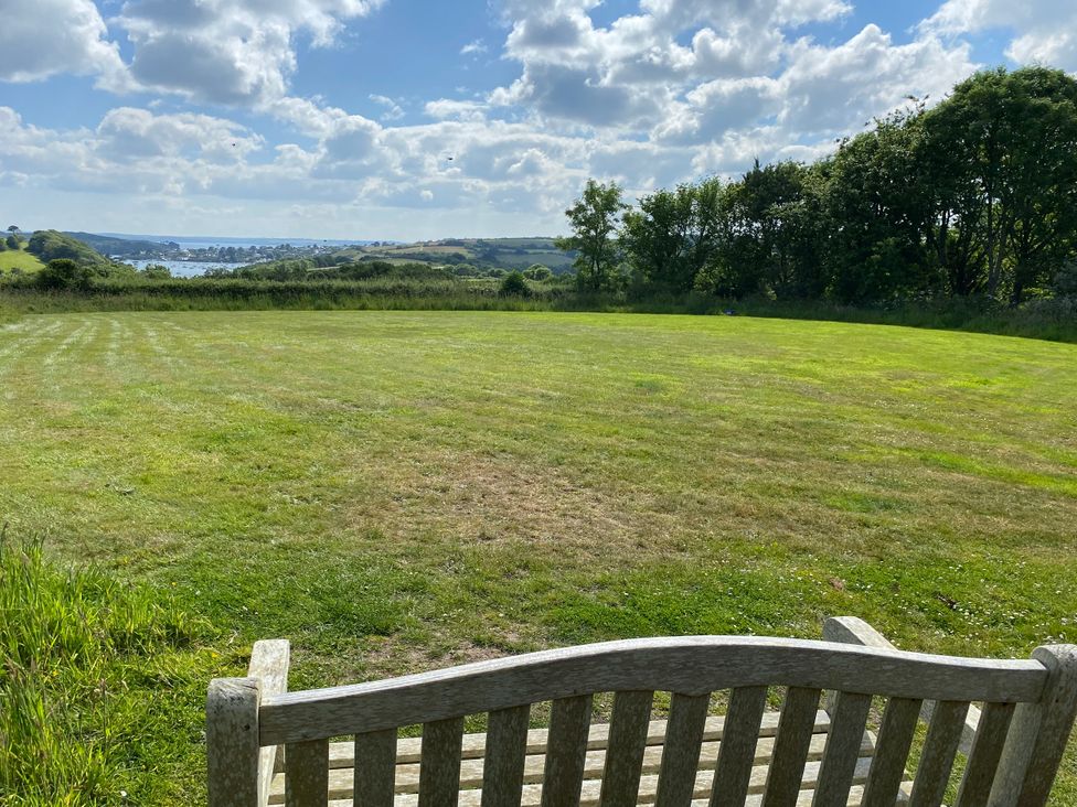 A view of grass and trees with a bench overlooking water at The Cowshed in Portscatho