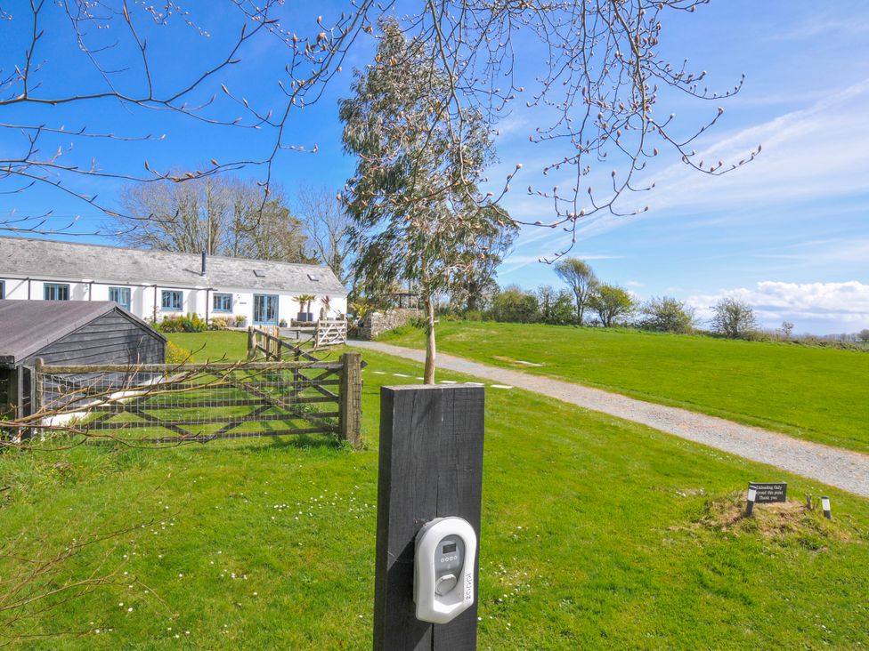 An outdoor view of a farmhouse with a gate and gravel path at The Cowshed in Portscatho