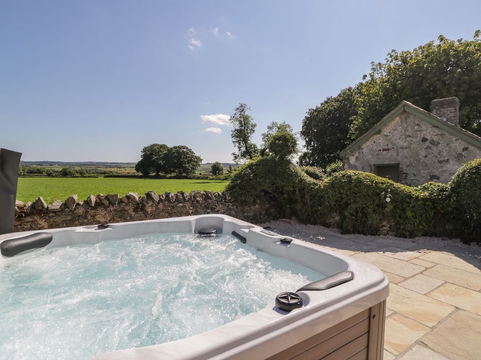 A hot tub next to a stone wall with a view of trees and fields at Ty Mawr Farm Llanfairpwllgwyngyll