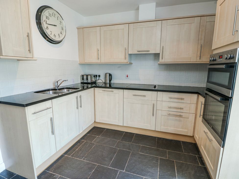 A kitchen with cabinets, sink, oven, and clock at Too Hoots in Lligwy
