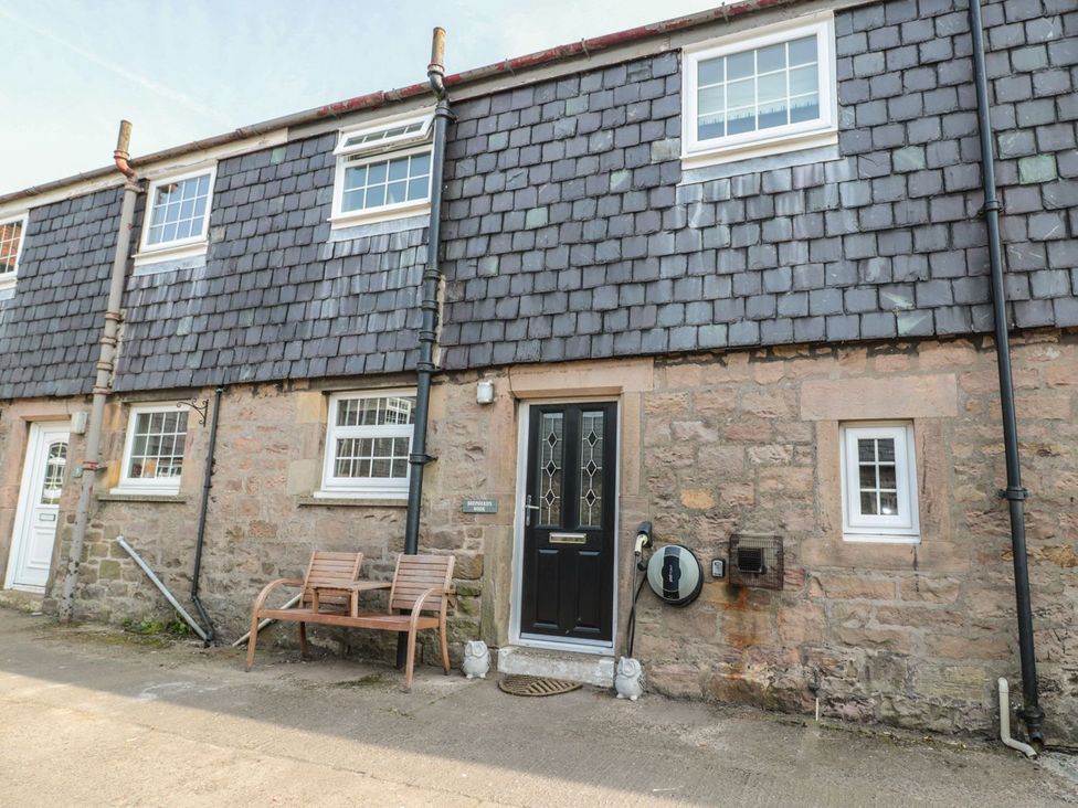 An outdoor view of a cottage with a bench and door at Shepherds Nook in Chathill
