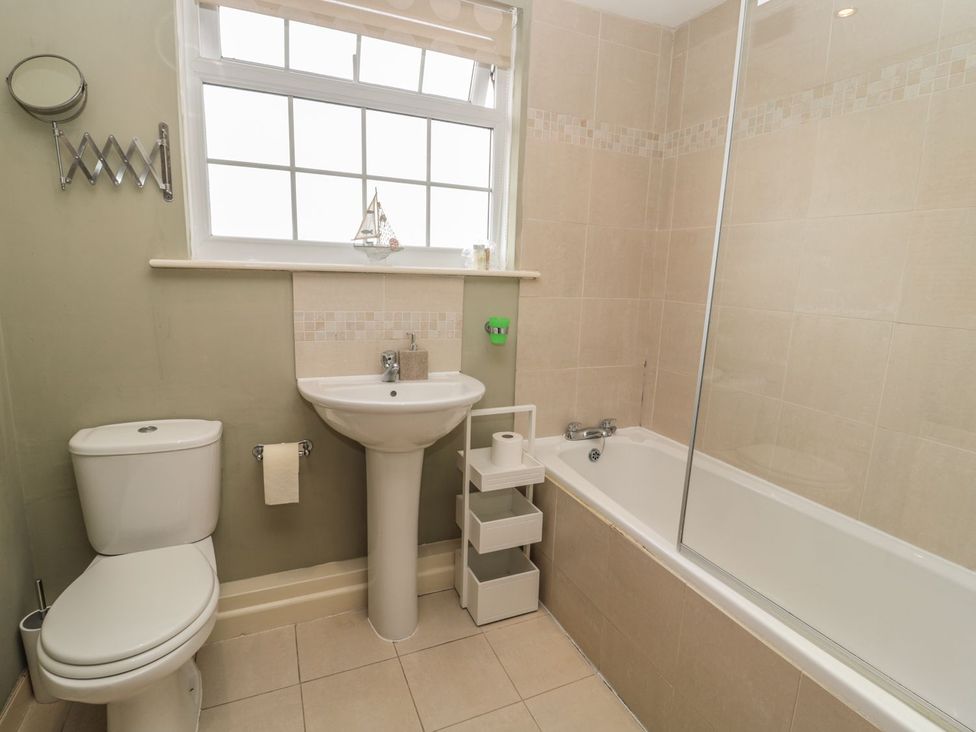 A bathroom with a sink, toilet, bathtub, and shelf at Shepherds Nook in Chathill