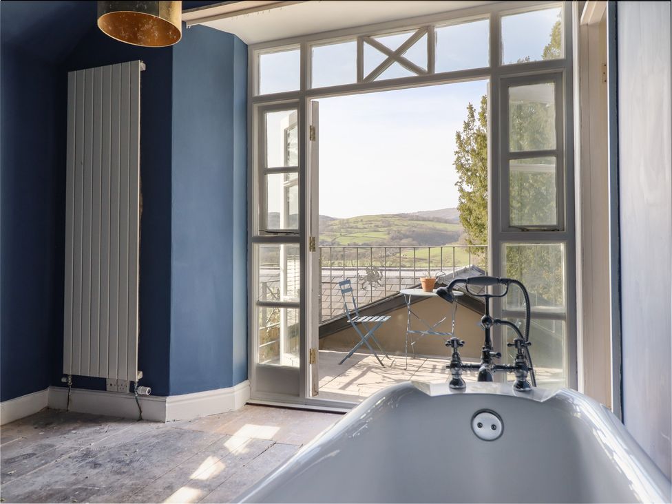 A bathroom with a bathtub and view to an outdoor balcony at Plas Dolguog in Machynlleth