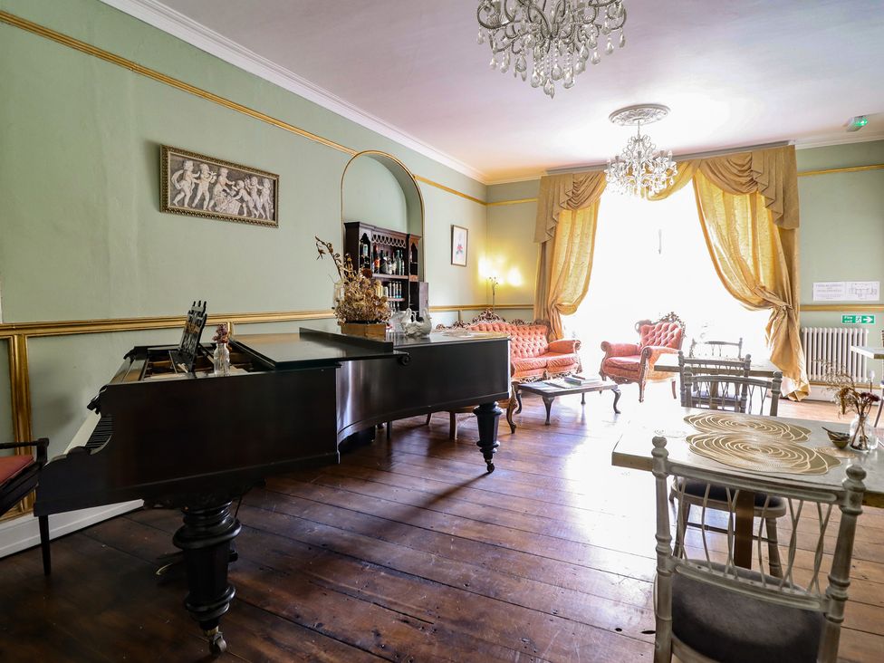 A lounge with a piano and seating at Plas Dolguog in Machynlleth