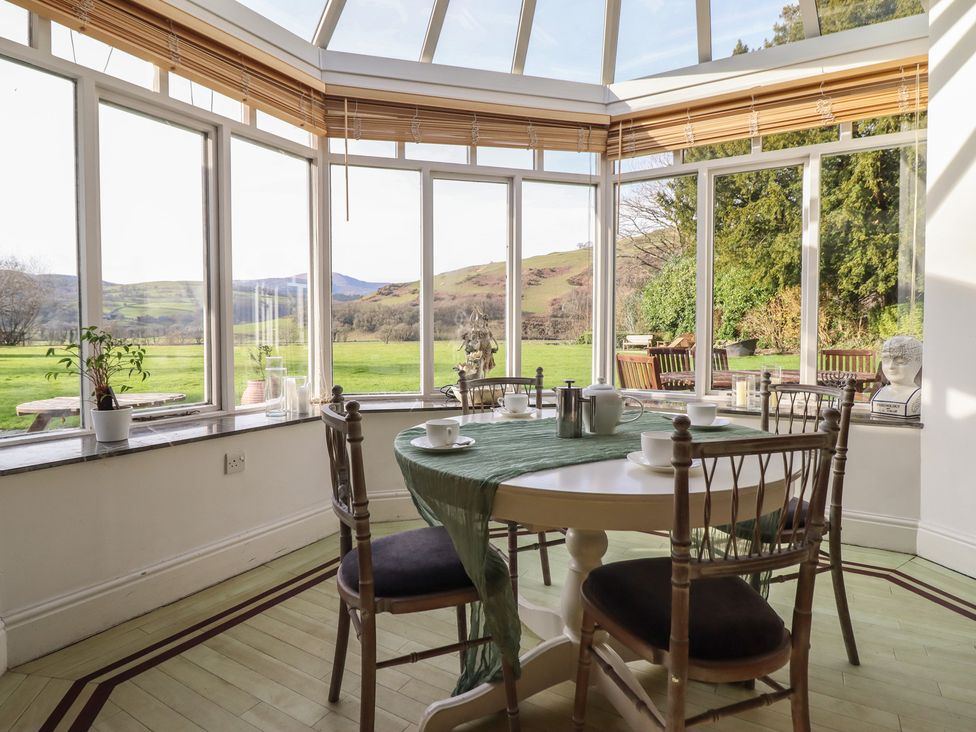A conservatory with a table and chairs overlooking a garden at Plas Dolguog in Machynlleth