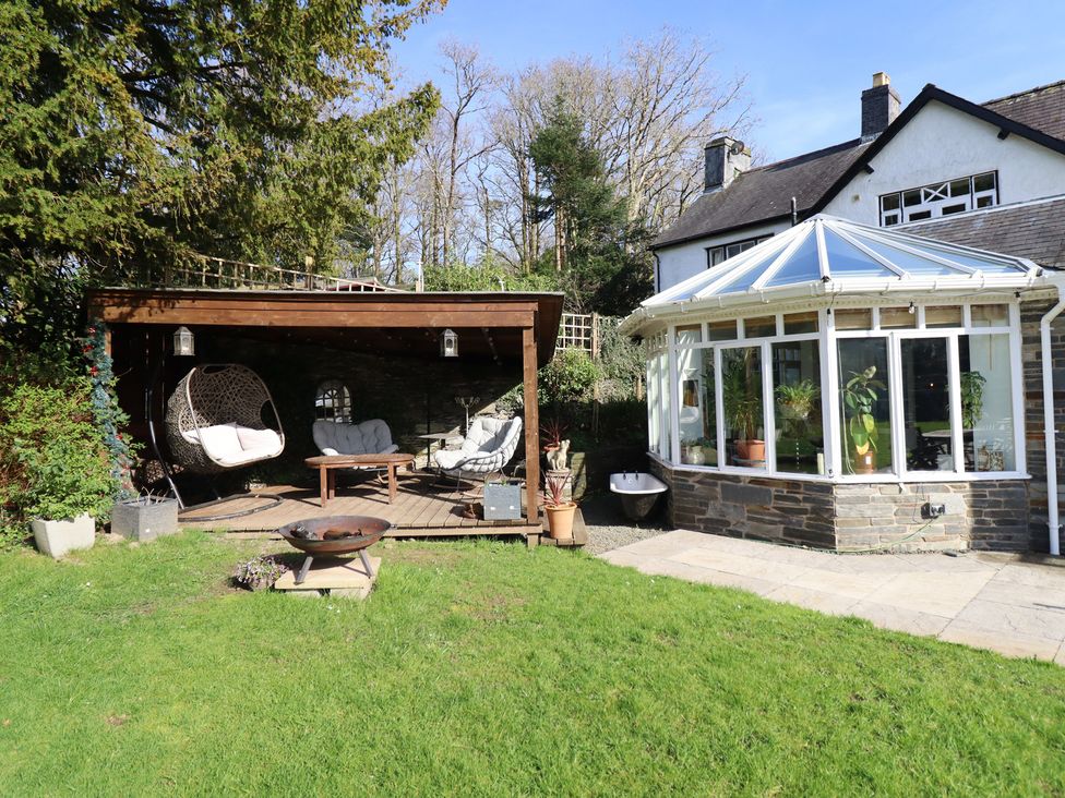 A garden with a wooden deck and glass conservatory at Plas Dolguog in Machynlleth