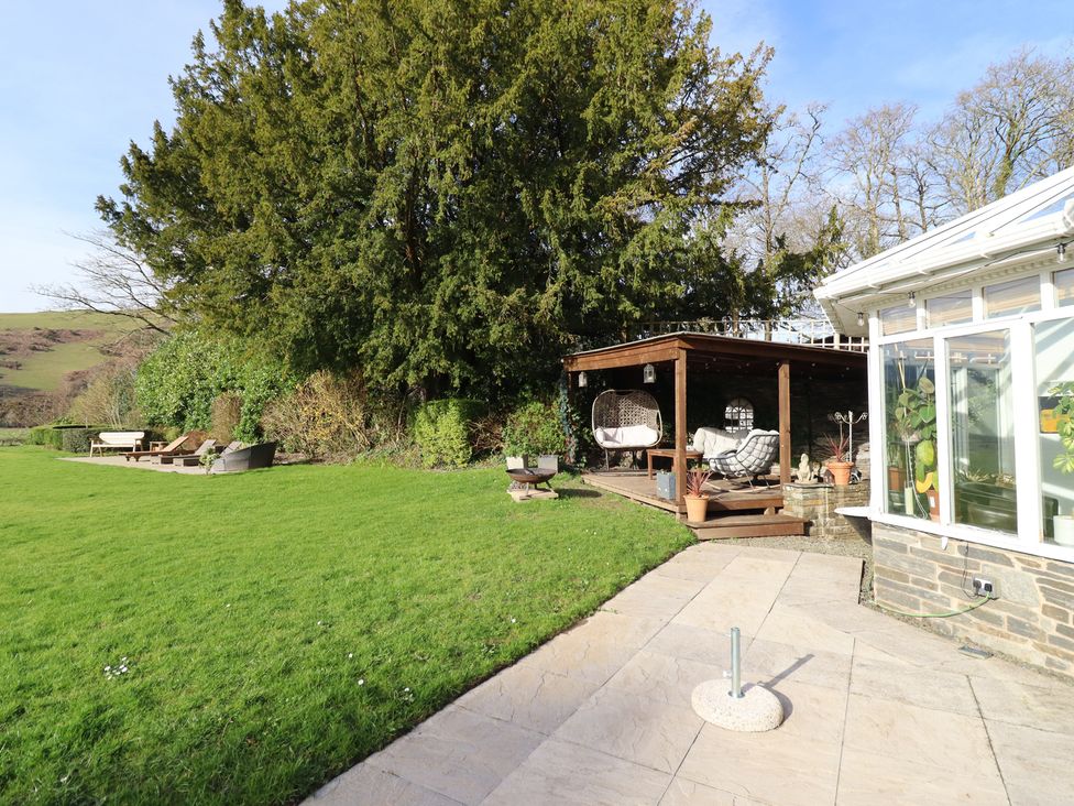 A garden with a pathway, deck, and hanging chair at Plas Dolguog in Machynlleth