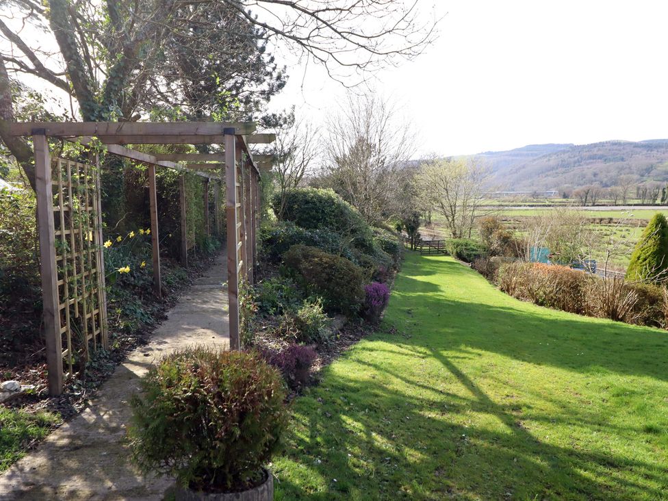 A garden with a pathway and trellis at Plas Dolguog in Machynlleth