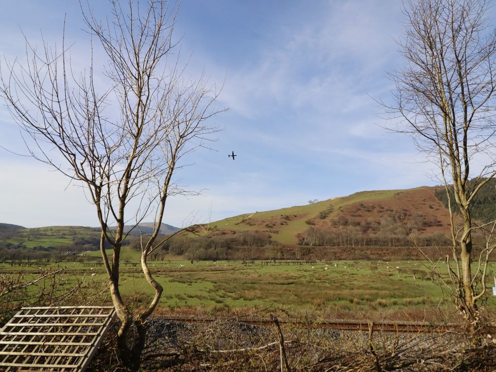 A landscape with trees and a plane flying over hills at Plas Dolguog in Machynlleth