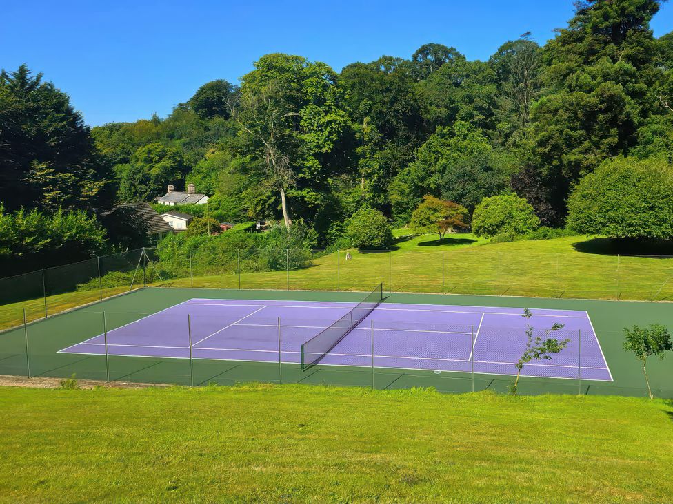 A tennis court surrounded by trees and grass at Lakeview Villa near Liskeard