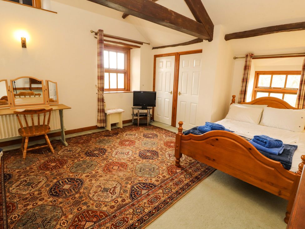 A bedroom with a bed, television, and dressing table at High Mill House in Penrith