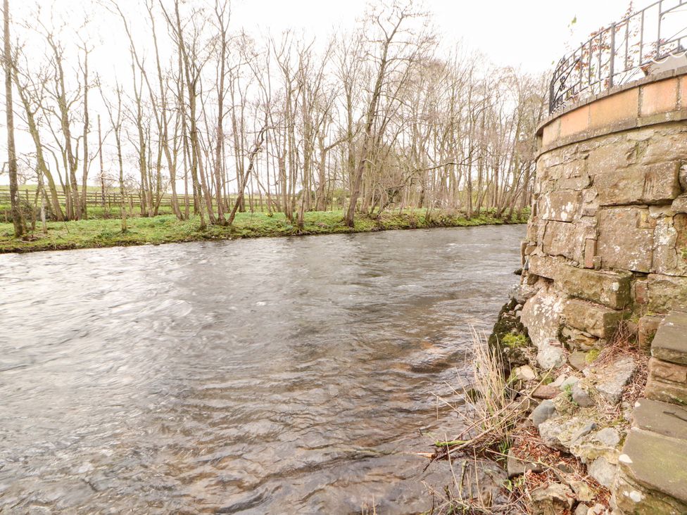 A river with trees and a stone wall at High Mill House Penrith