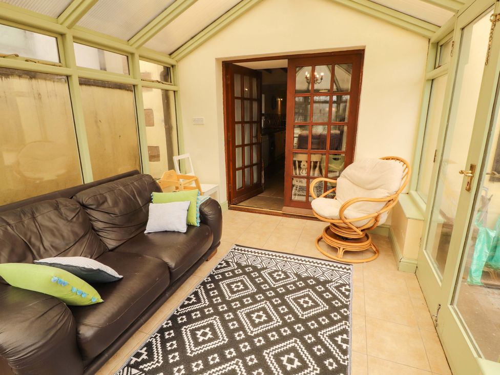 A conservatory with a couch and dining table at High Mill House in Penrith