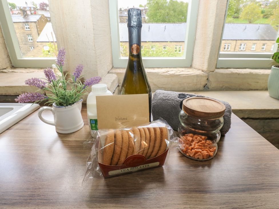 A kitchen countertop with champagne, biscuits, milk, and a flower pot at Riverview Cottage in Holmfirth