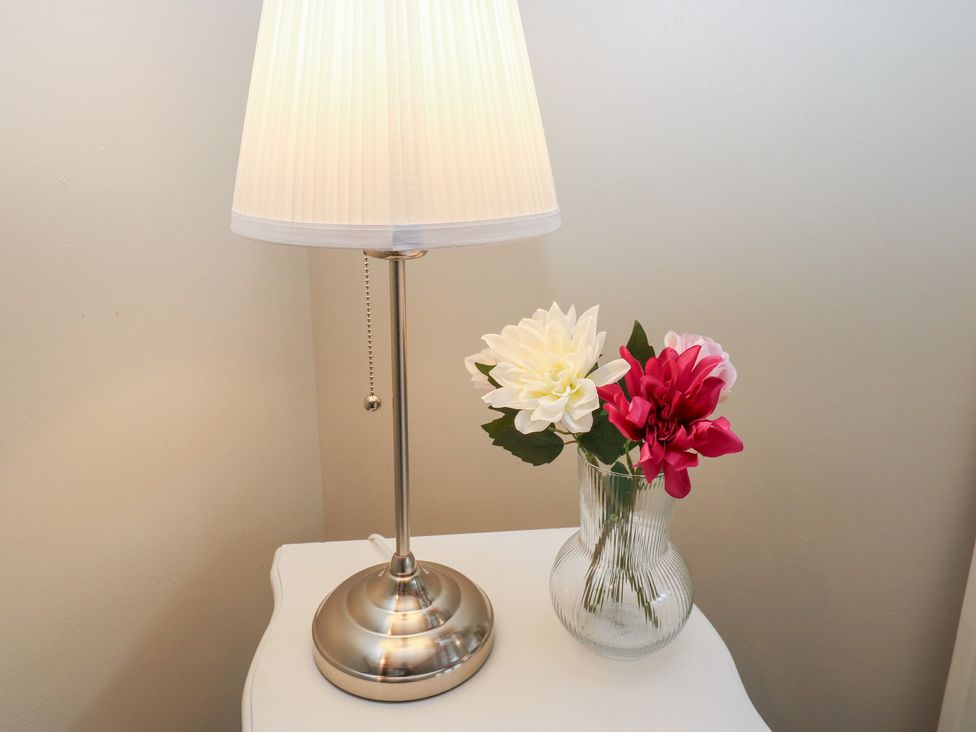 A lamp and a vase with flowers on a table at Riverview Cottage in Holmfirth