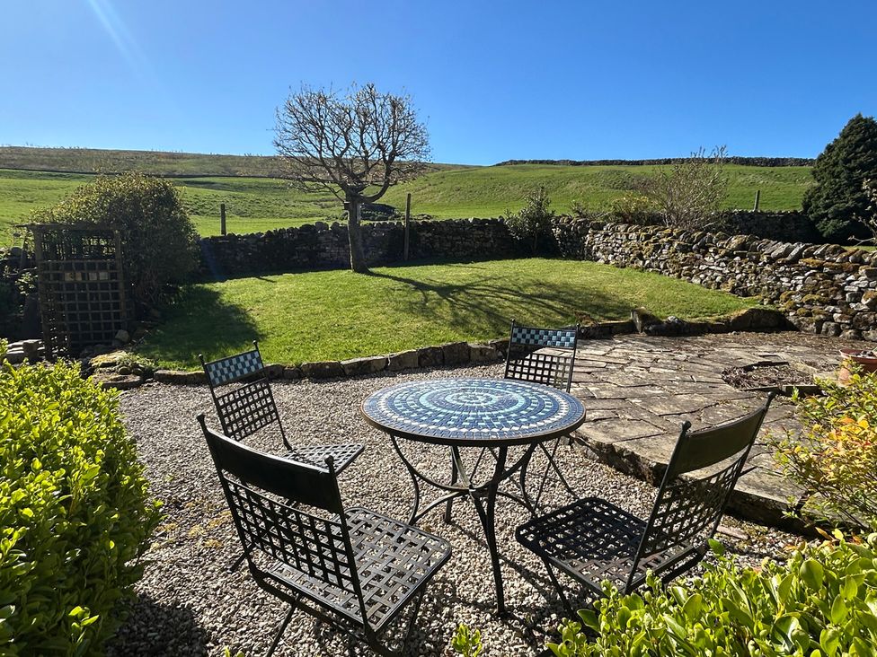 A garden with a table and chairs in the sun at Tarn House in Hawes