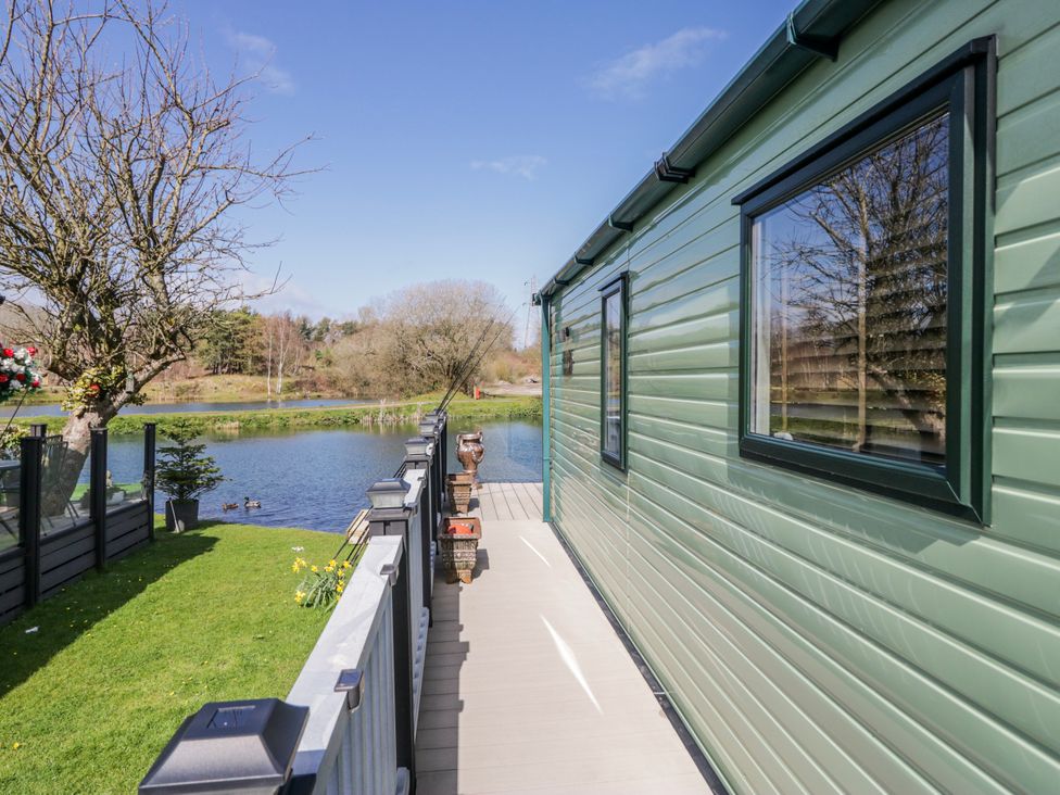 A house by a river with a deck and grass area at Carp Lodge