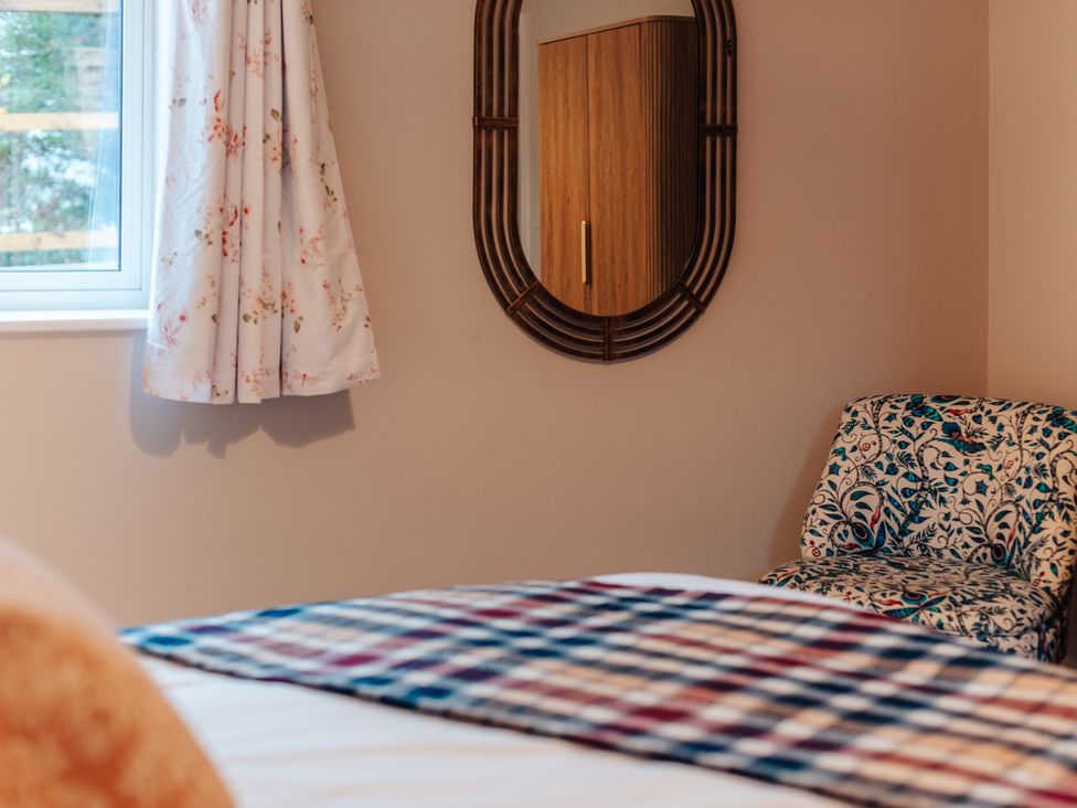 A bedroom with a window, curtain, mirror, cabinet, and chair at The Stables in Catworth