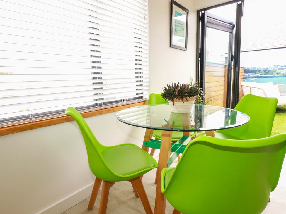 A dining room with glass table and green chairs at La Casita Newquay