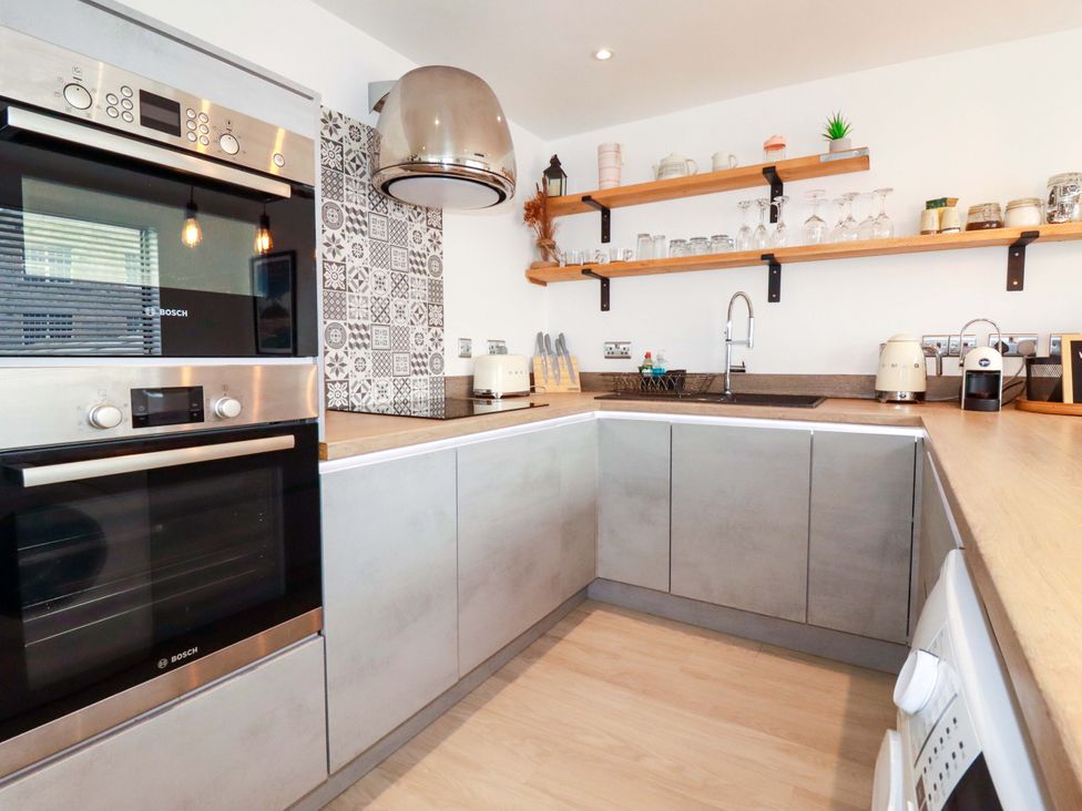 A kitchen with an oven, microwave, sink and shelves at La Casita in Newquay