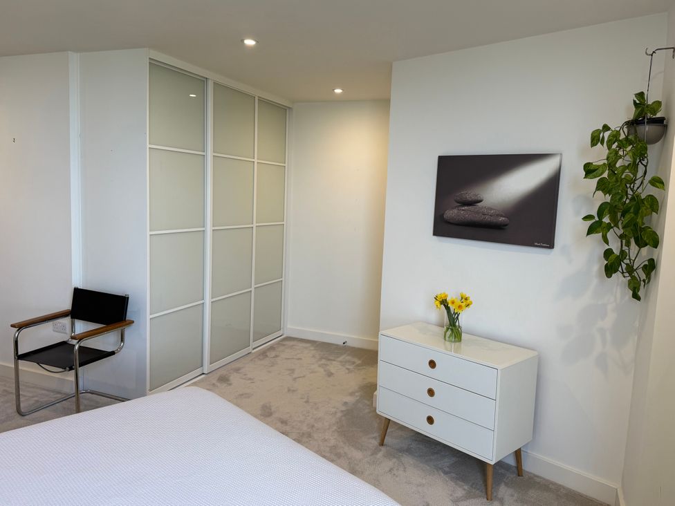 A bedroom with a bed, chair, dresser and closet at Apartment 29 in Newquay