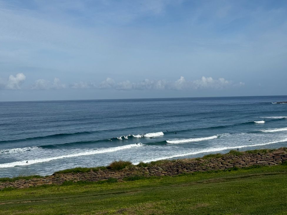 A view of the ocean with surfers and a stone wall at Apartment 29 in Newquay