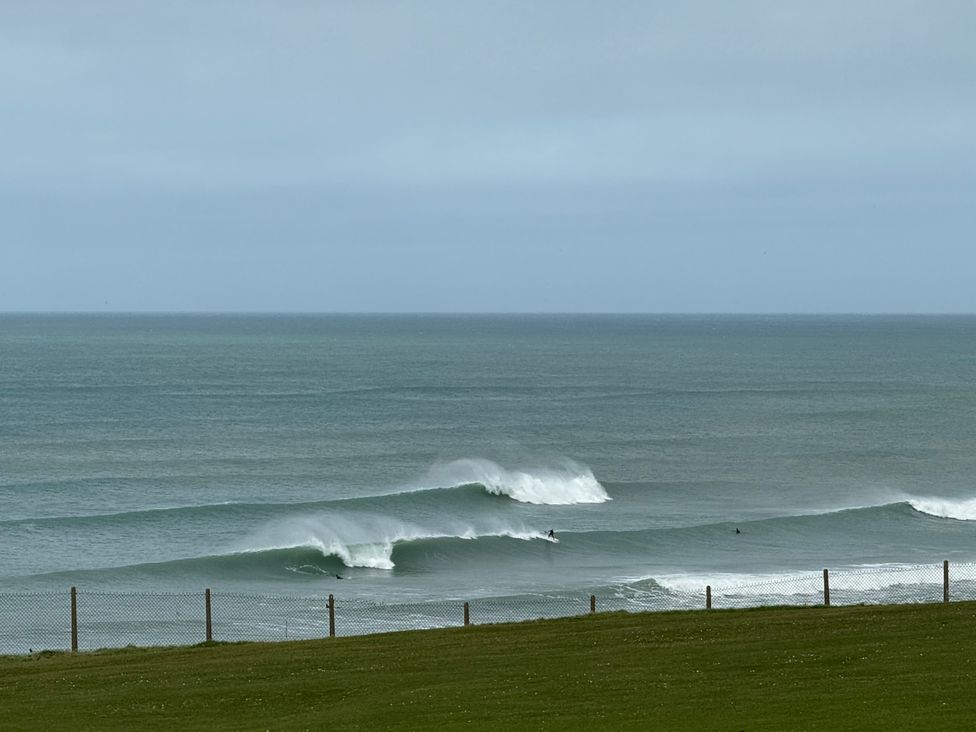 An ocean with waves and surfers near a grass area at Apartment 29 Newquay
