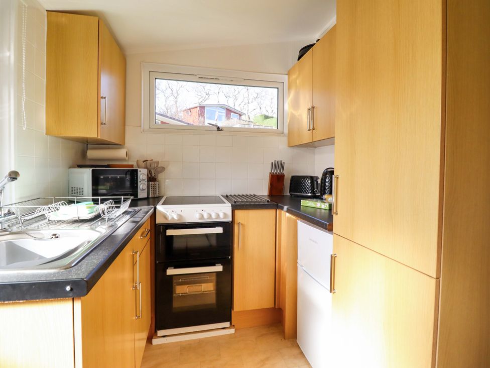 A kitchen with a sink, oven, microwave, and cupboards at Chalet 23 Erw Porthor Tywyn