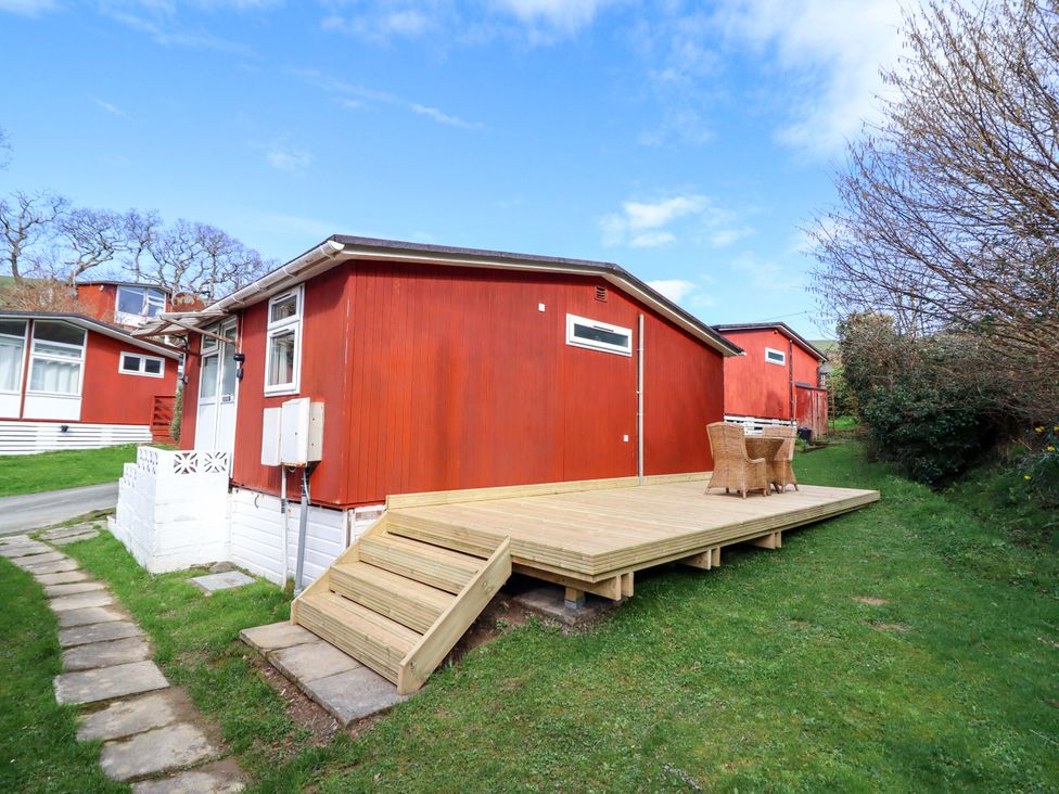 A red cabin with wooden deck and outdoor seating at Chalet 23 Erw Porthor Tywyn