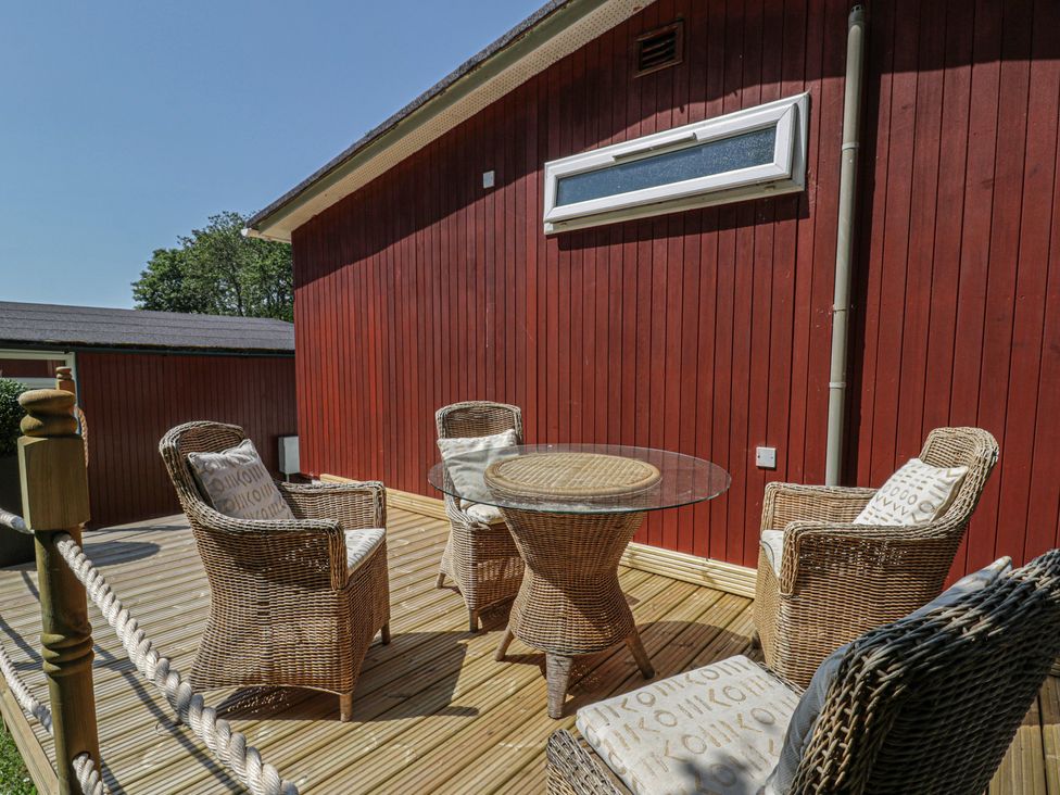 A patio area with wicker furniture and a glass table at Chalet 23 Erw Porthor Tywyn