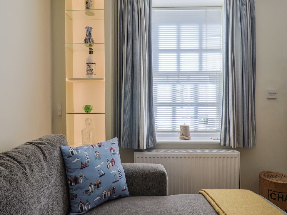 A living room with a couch and decorative items on a shelf at Phoenix Cottage in Lyme Regis