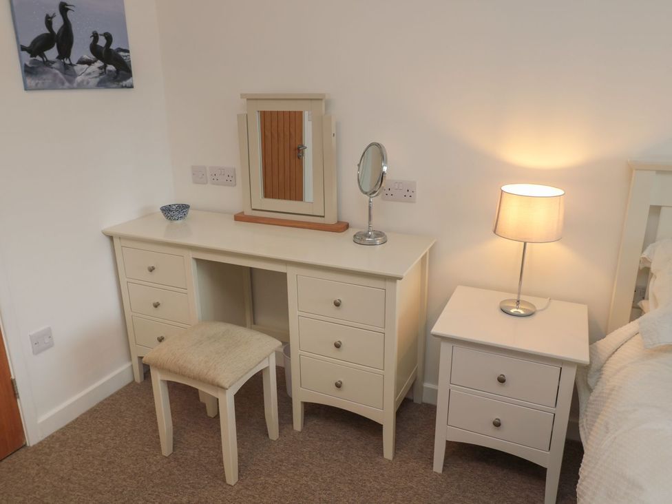 A bedroom with a vanity table, mirror, lamp, and nightstand at 7 Longstone Close, Chathill