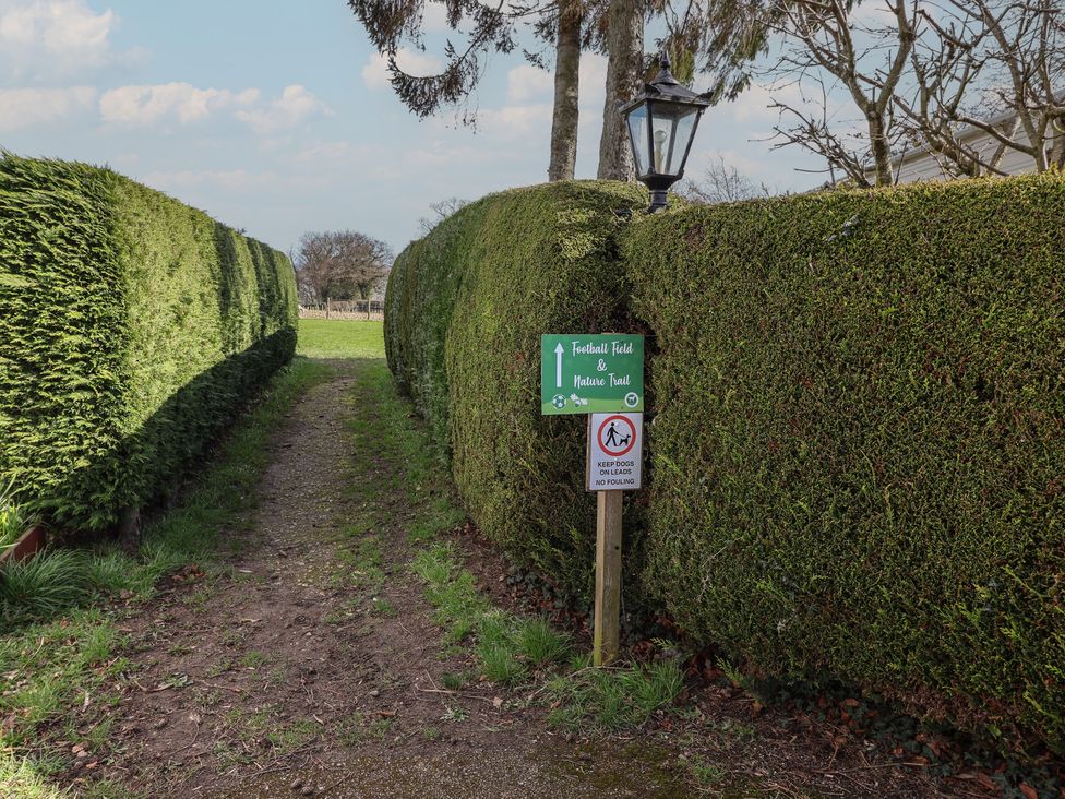 A path leading through hedges with signs for a football field and nature trail at Woodlands Hall Caravan Park near Ruthin